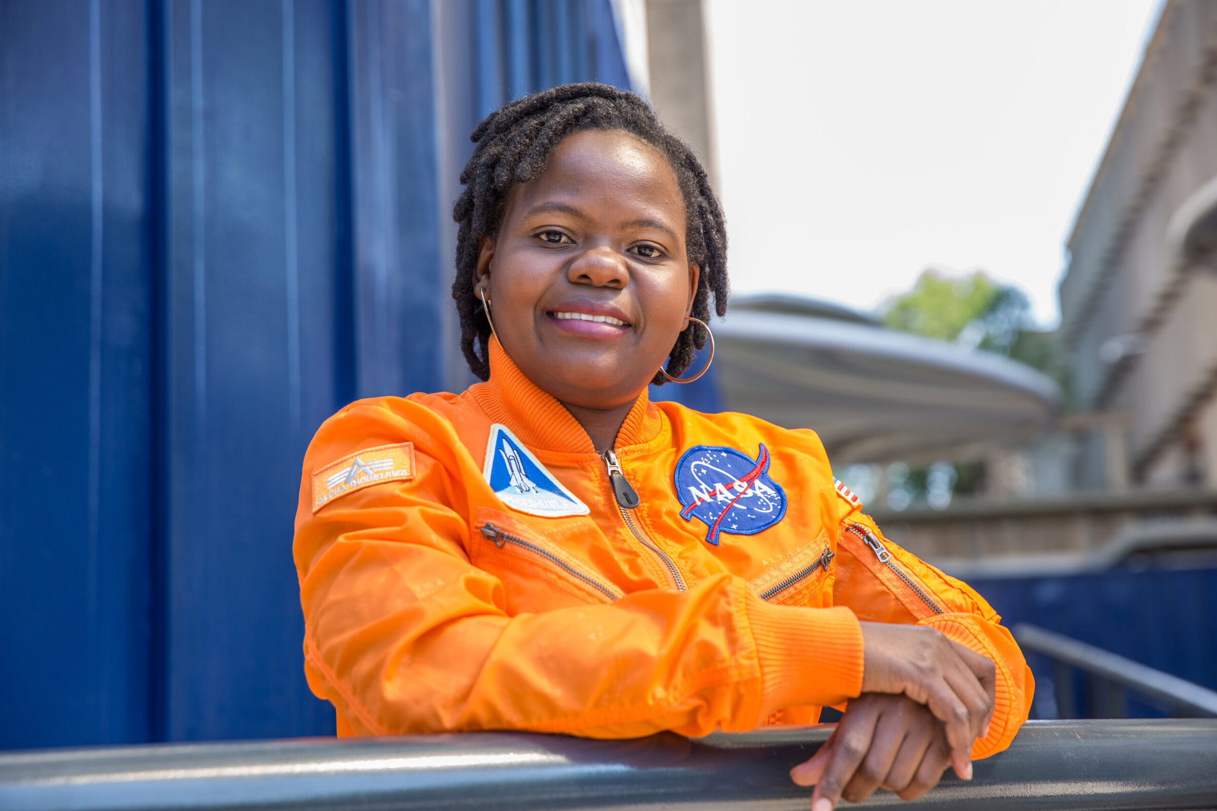 NASA astronaut in orange spacesuit smiling outdoors.