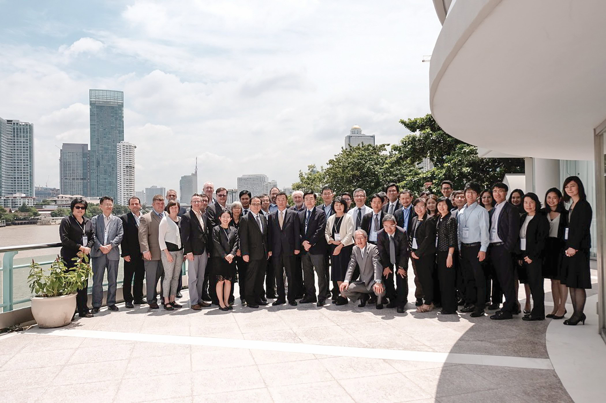 Large group of professionals at ceramics conference on outdoor balcony with city skyline in background.