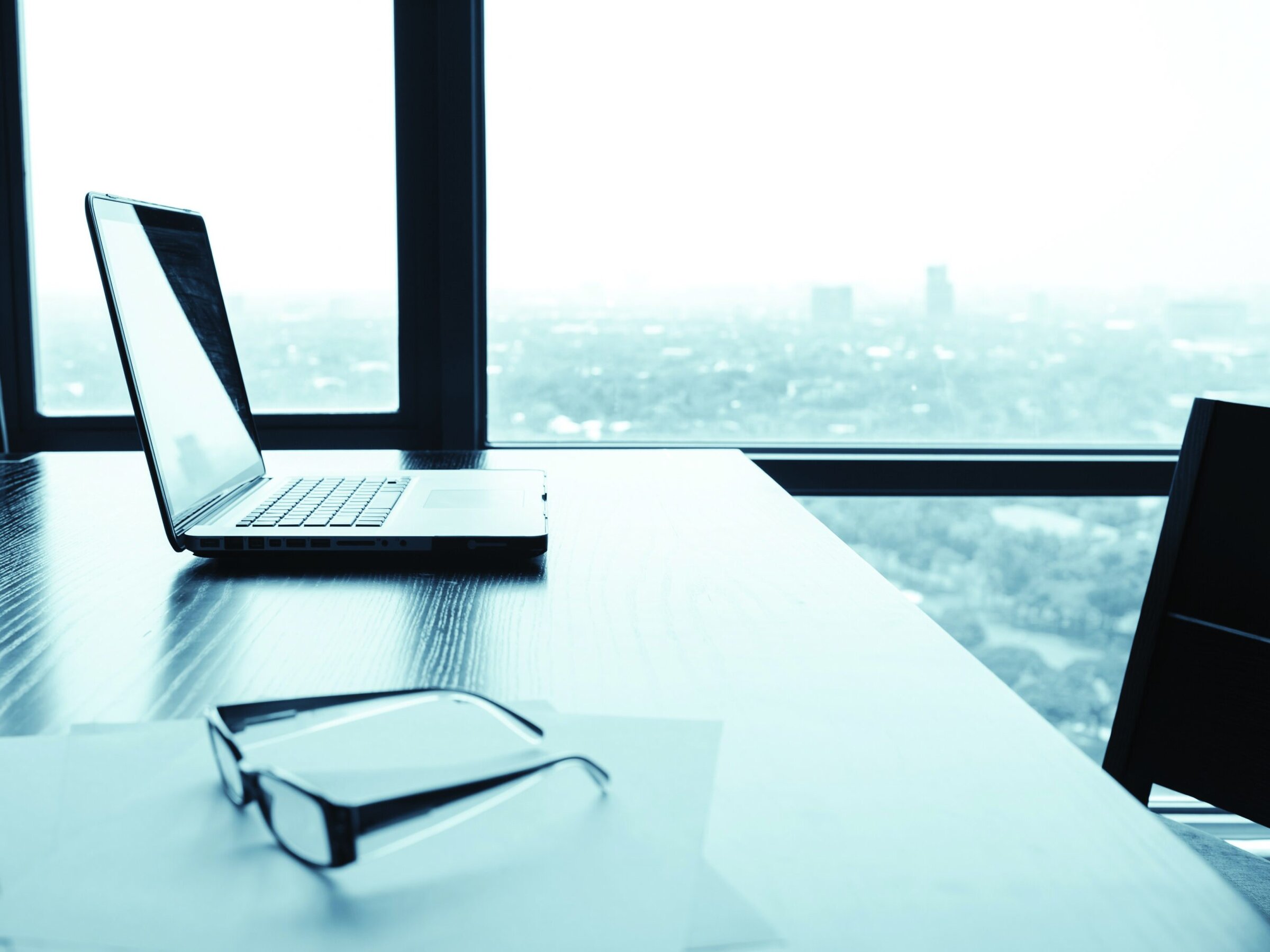 Laptop on a modern office desk with city views, professional workspace for ceramics industry leaders.