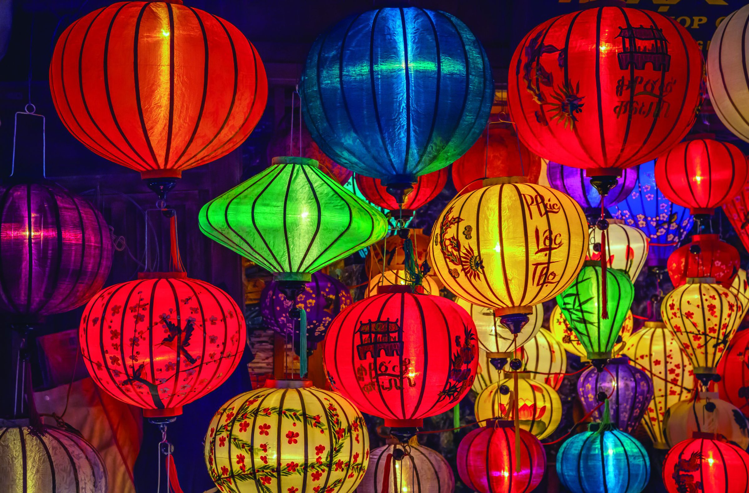Colorful paper lanterns in red, green, yellow, blue, and purple illuminate a night scene, showcasing traditional Asian festival decorations.