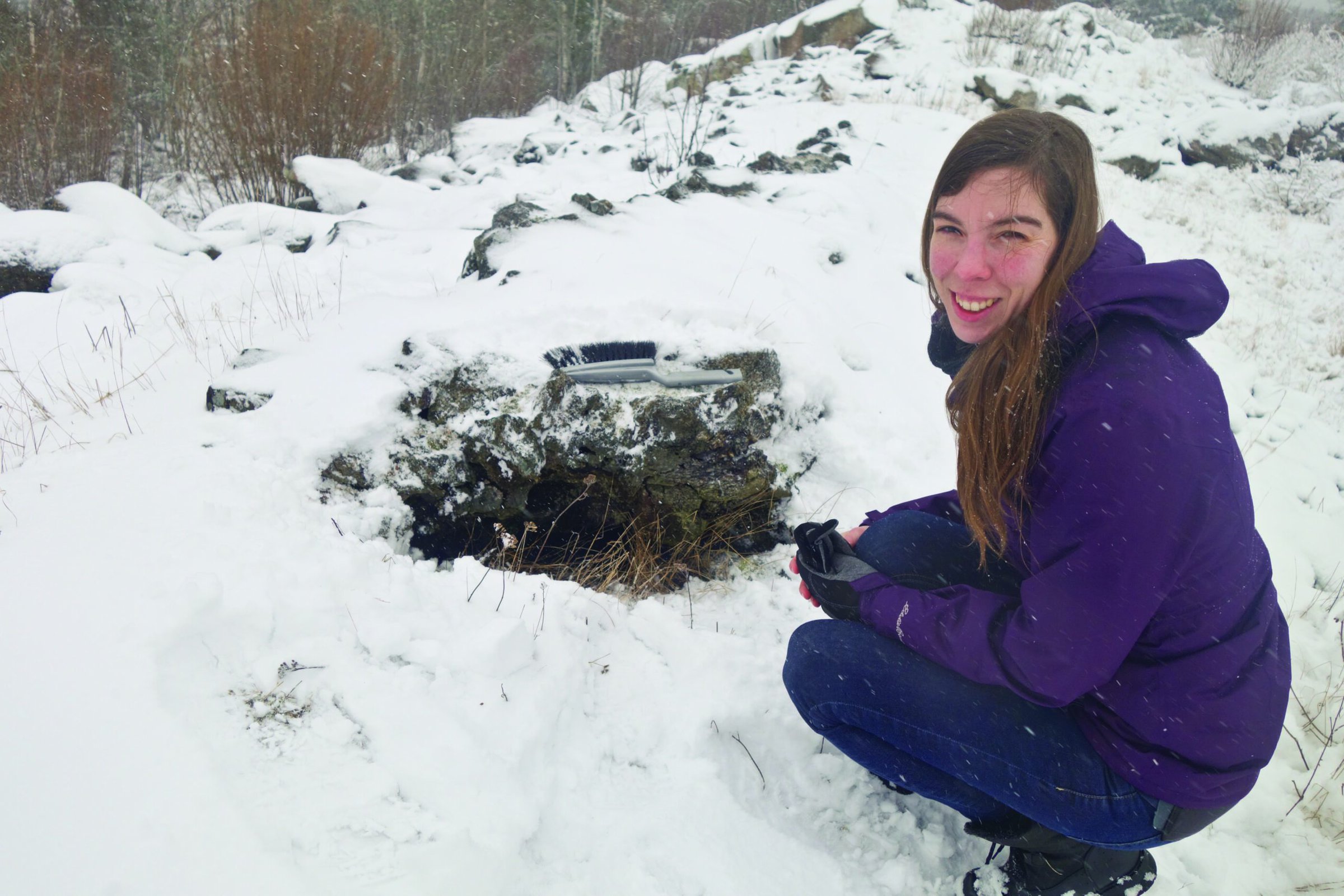 Snow-covered geological research site with a smiling woman in outdoor winter gear.