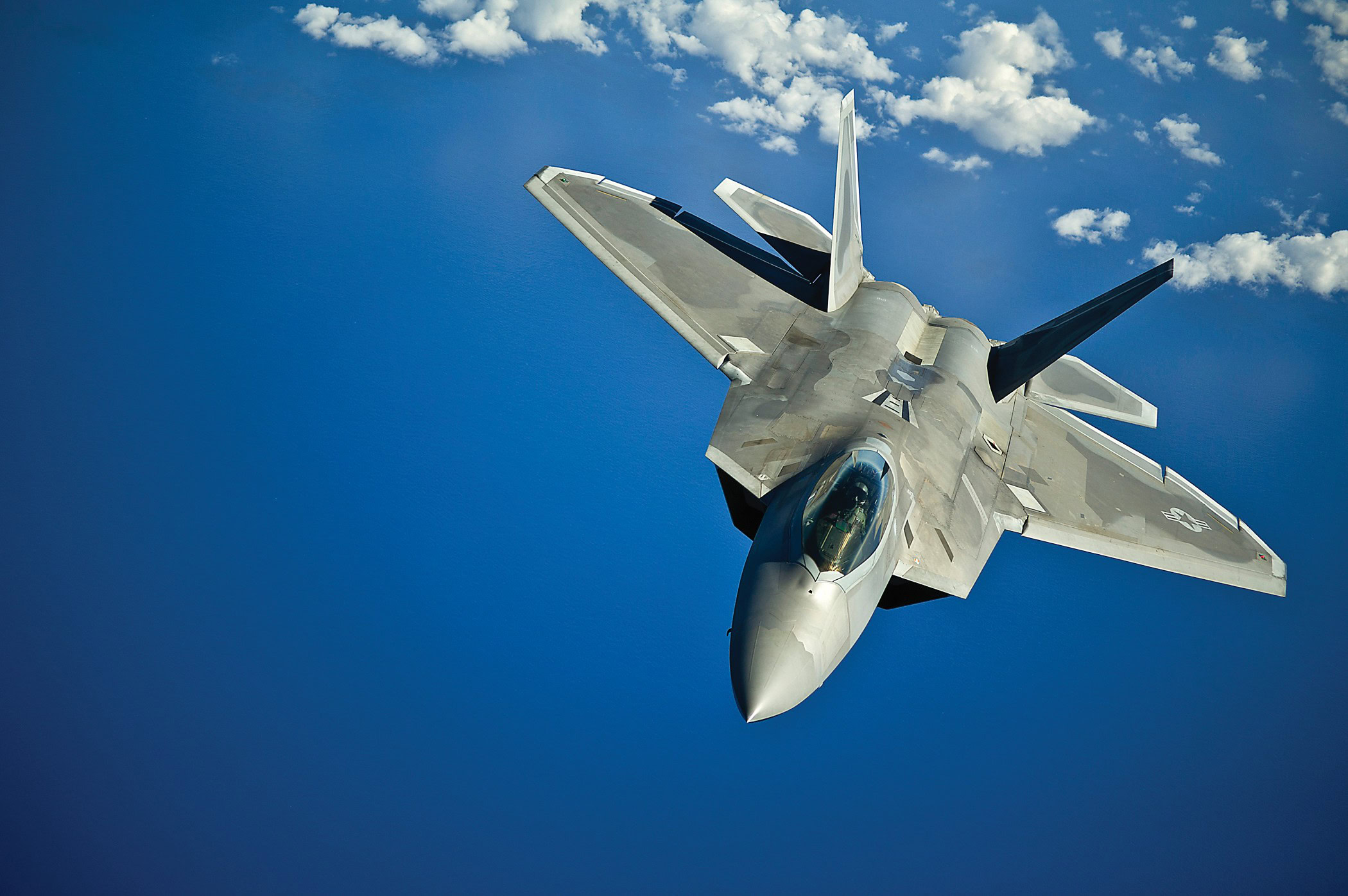 F-22 Raptor fighter jet soaring in blue sky with clouds, military aircraft, advanced weaponry, aviation technology, aerospace engineering.