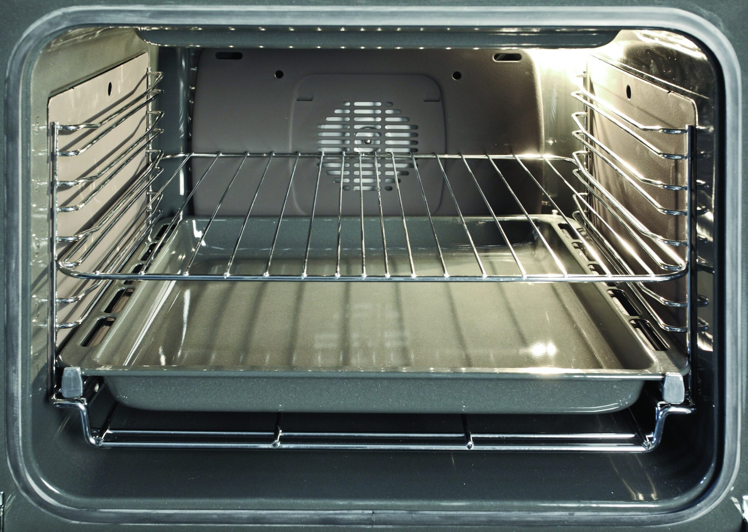 Shiny stainless steel oven interior with racks and tray, modern kitchen appliance for baking and roasting.