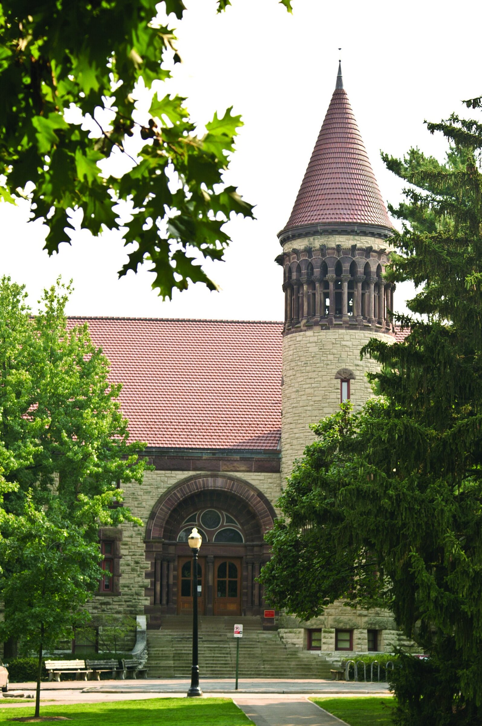 Historic castle with red tiled roof and stone walls, surrounded by lush greenery.