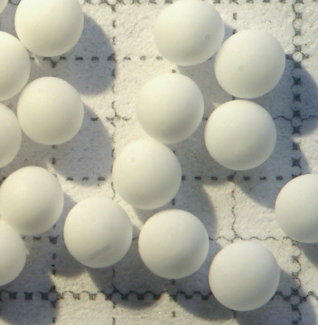 White ceramic balls on a textured surface, ideal for ceramics and materials science applications.