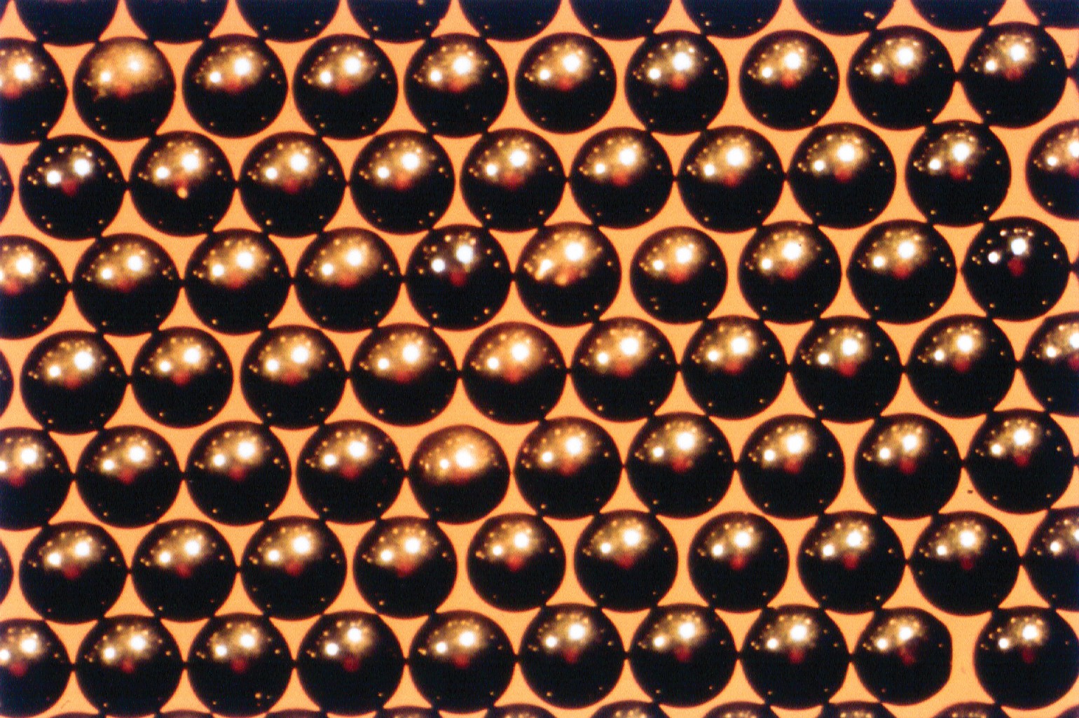 Glossy black ceramic spheres on orange background for ceramics and materials research.