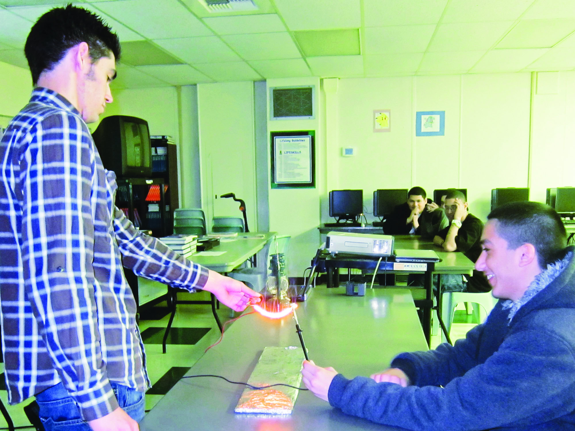 Young students conducting a science experiment with electrical components and glassware in a classroom setting.
