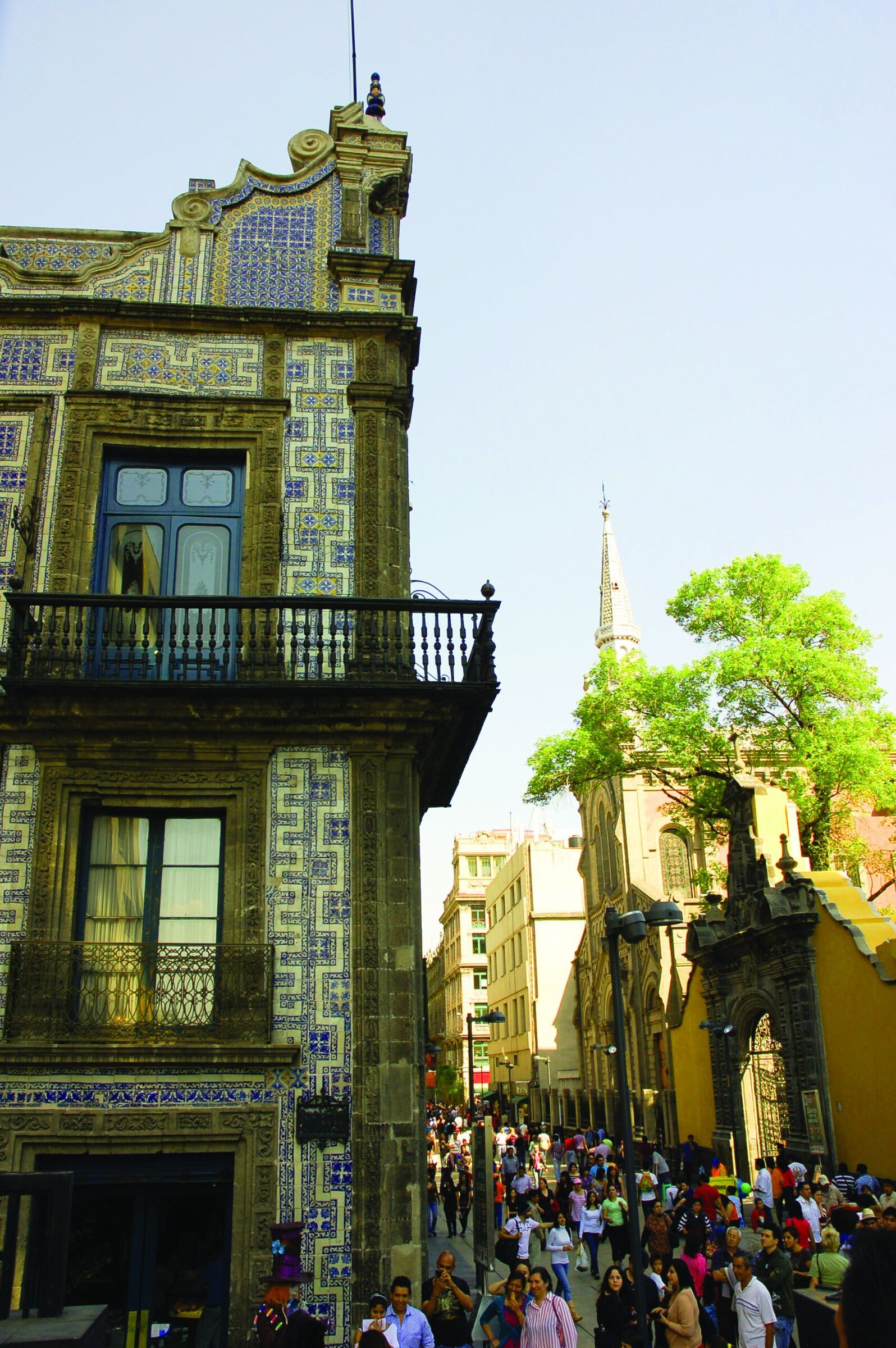 Vibrant street scene with colorful historic buildings, a church steeple, and a crowd of pedestrians in a lively urban area.