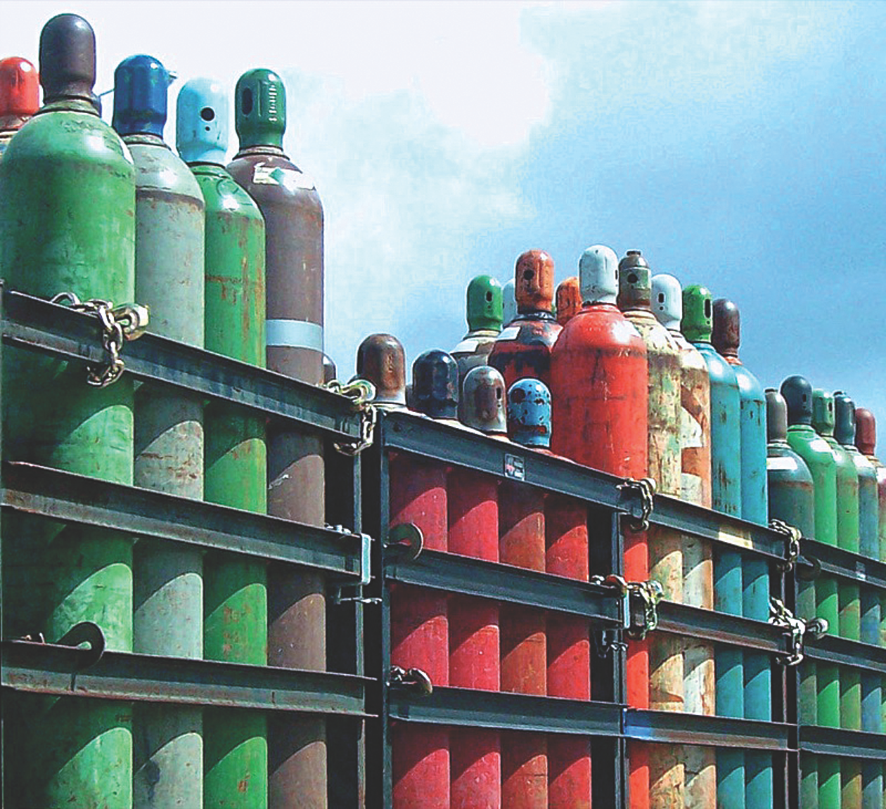 A colorful array of gas cylinders secured on a metal rack against a blue sky background.
