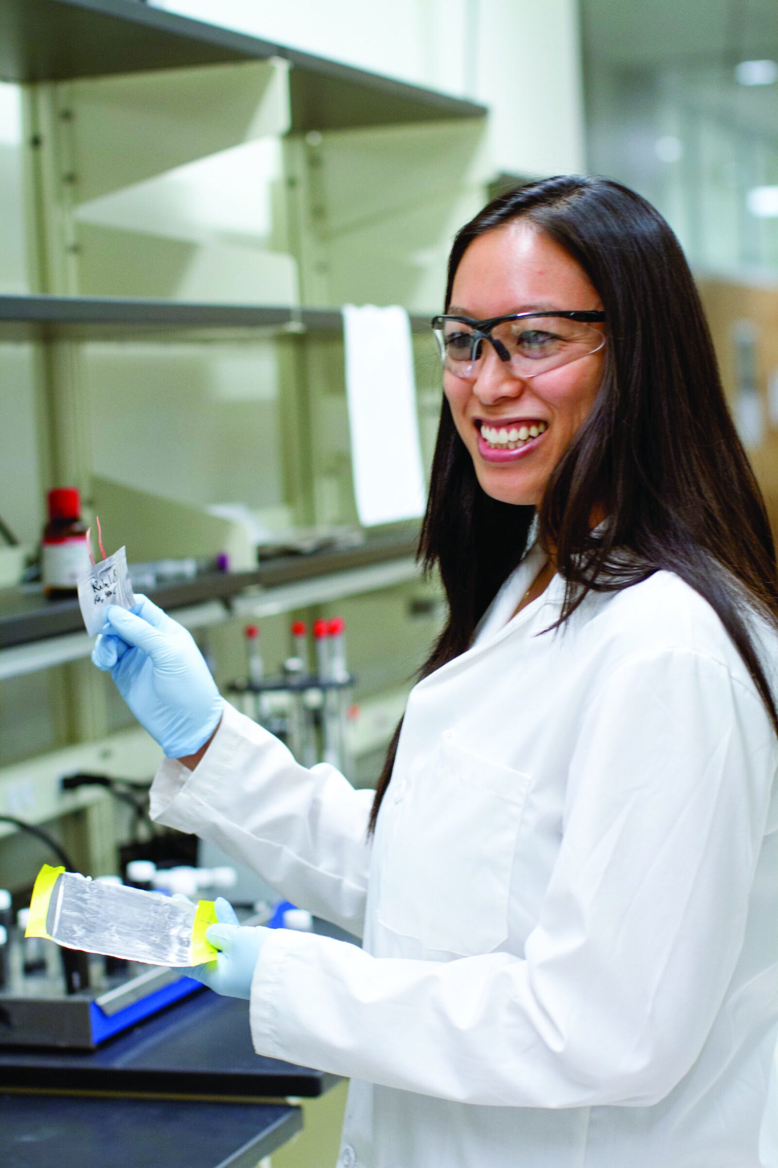 Woman in lab coat smiling with her research.