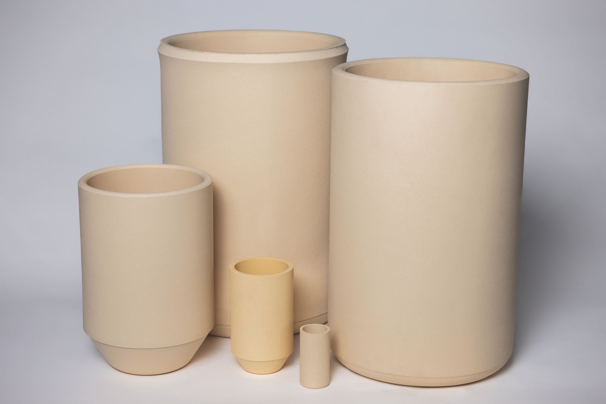Tan crucibles shaped like cylinders against a gray background.