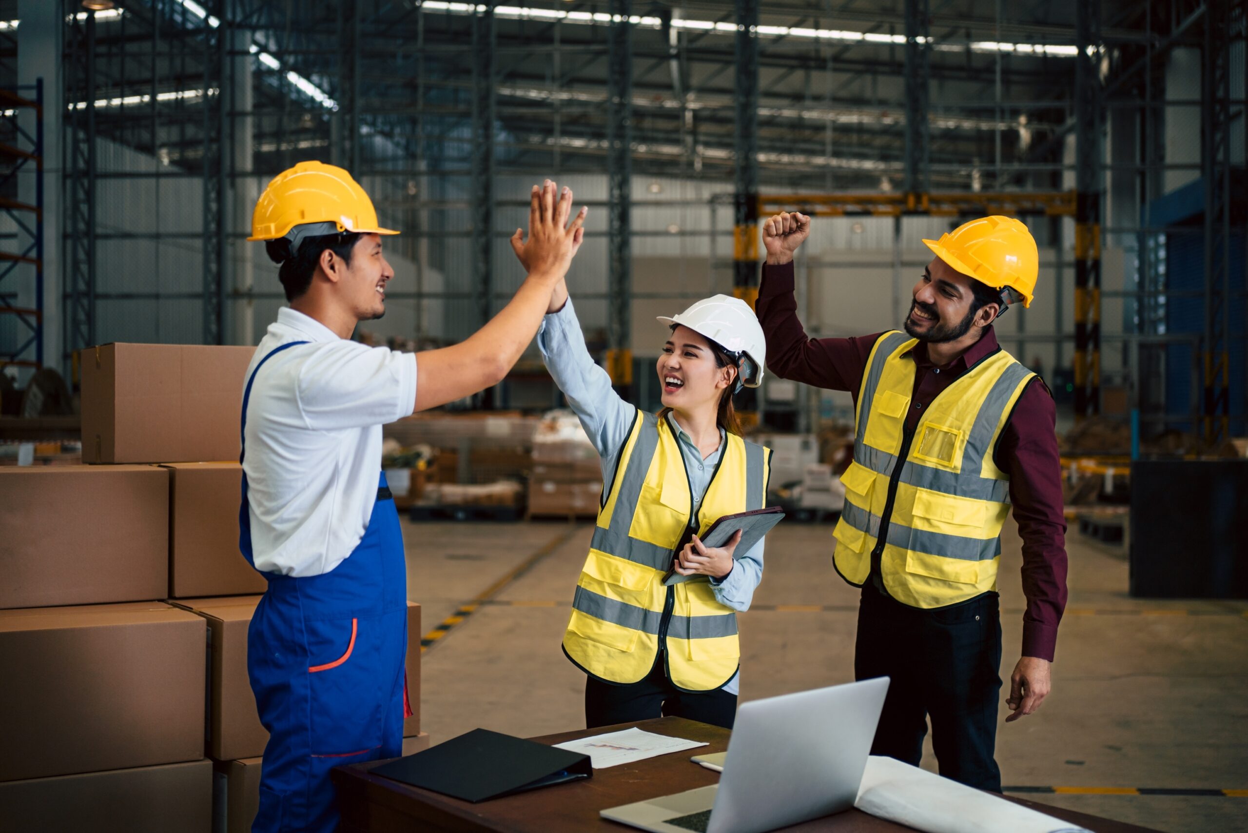 Group of three engineers in yellow vests high-fiving in a factory setting.