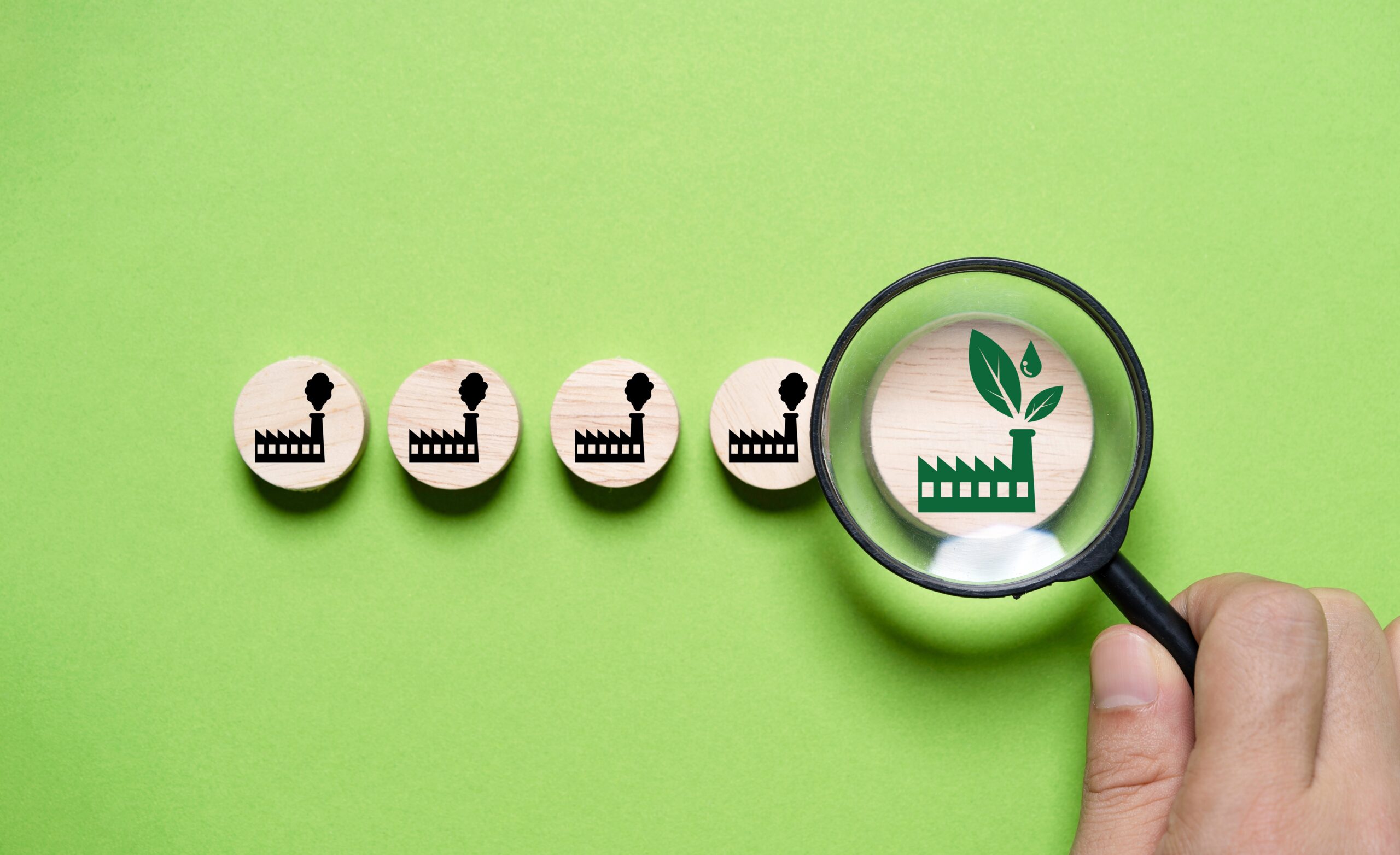 A person holds a magnifying glass over a green glass icon with leaves, symbolizing sustainability and eco-friendly practices