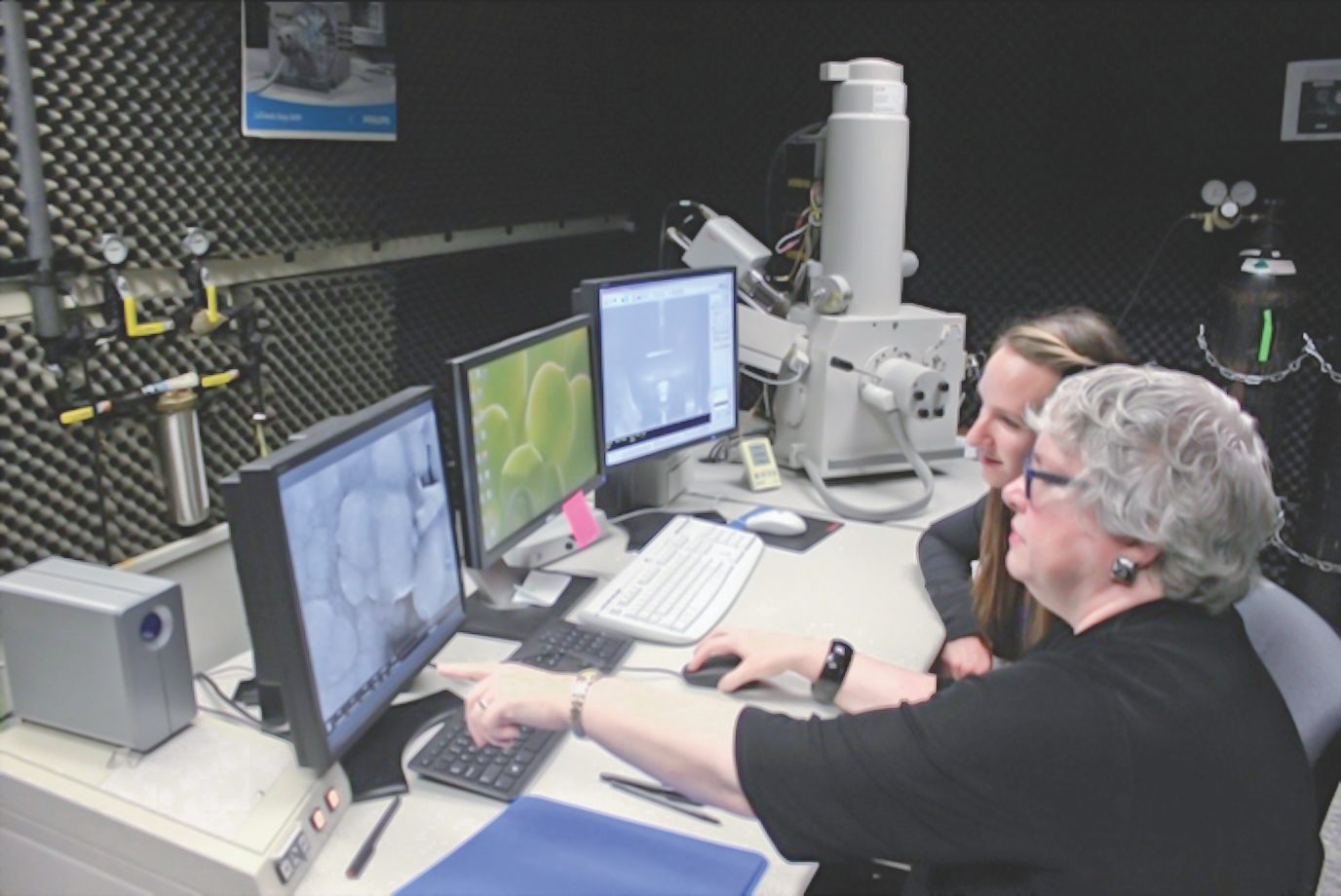 High-tech laboratory with two women analyzing materials on multiple computer screens in a research setting.