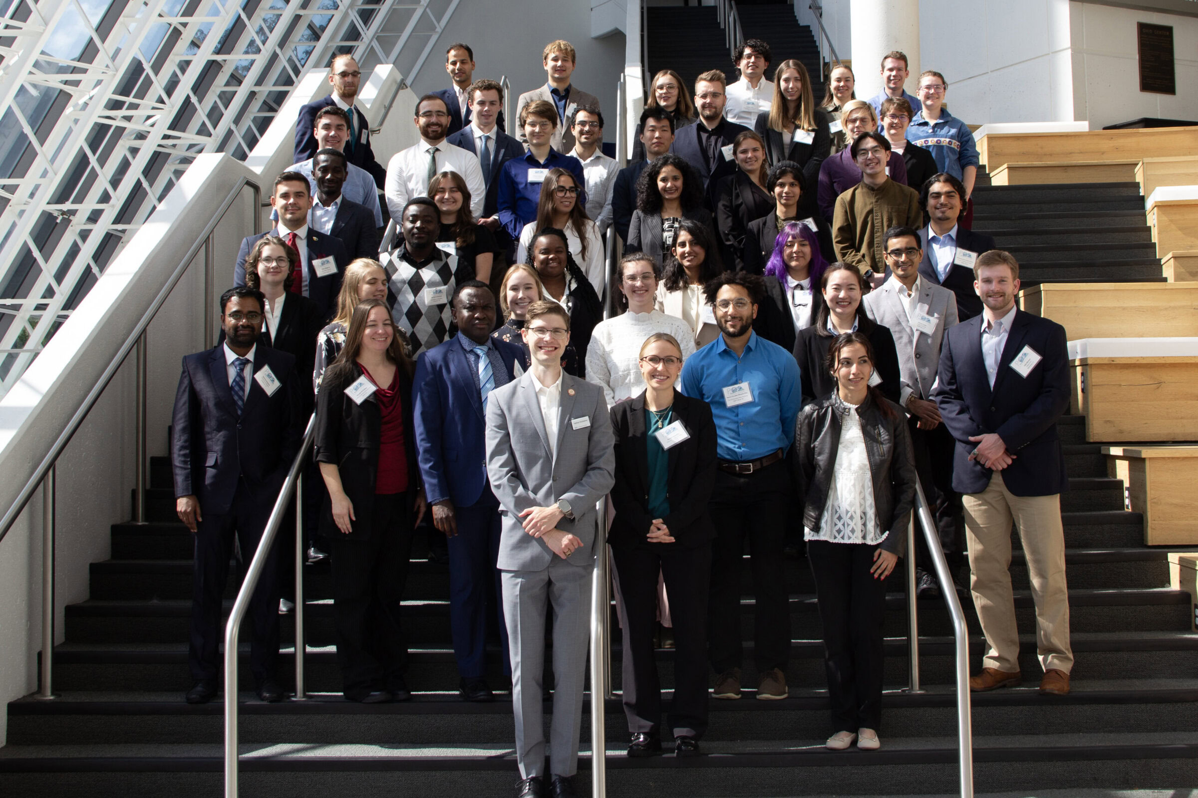 A diverse group of professionals and students posing on a staircase at a conference or event.