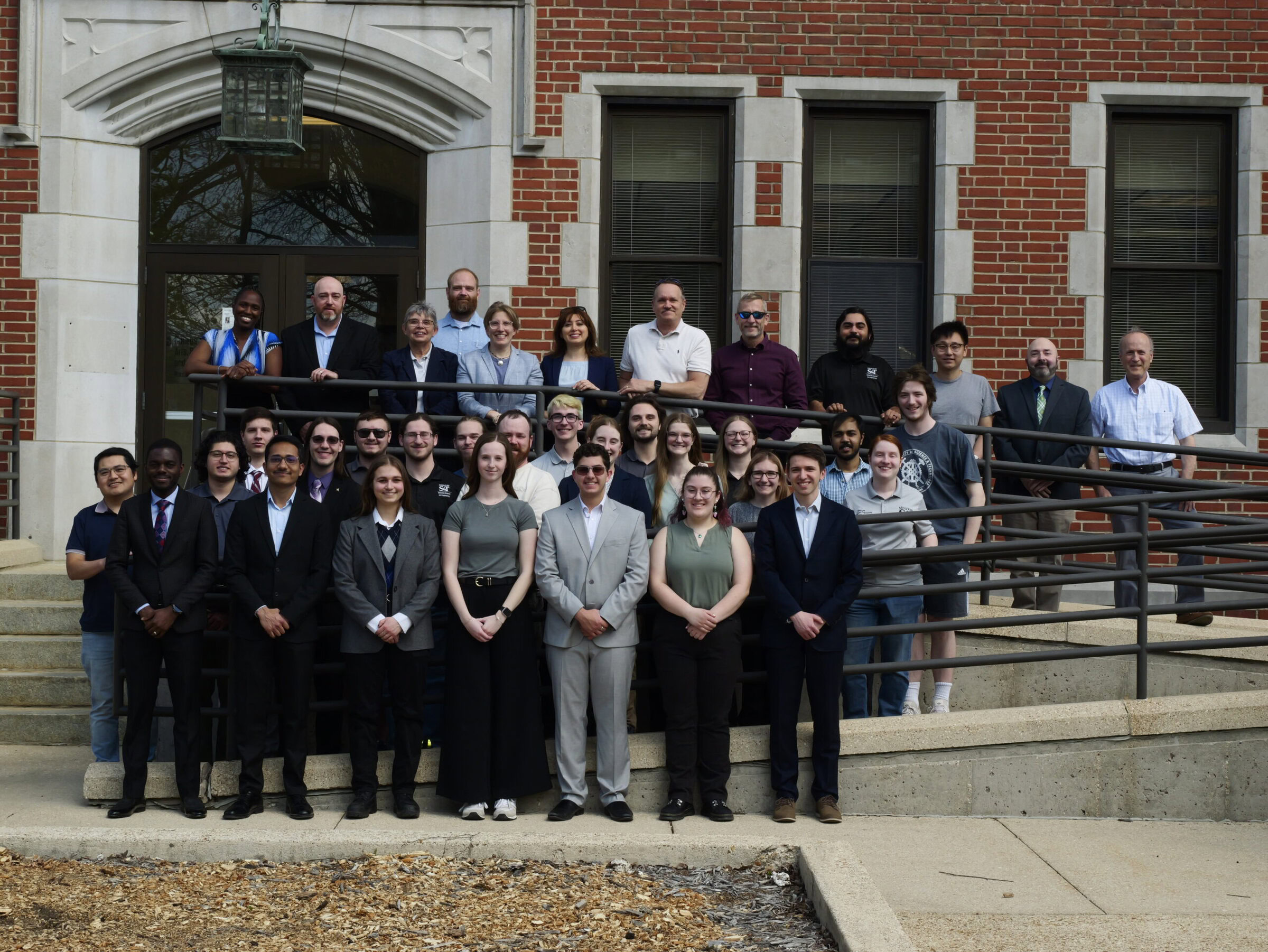 A diverse group of professionals standing on the steps of a brick building, posing for a group photo outdoors.