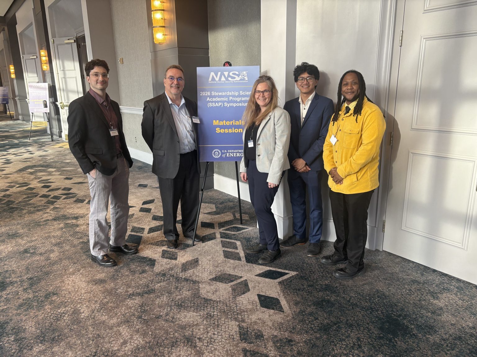 Diverse group of five professionals standing together at a conference, smiling, with a sign for the 2023 Scholarship Session.