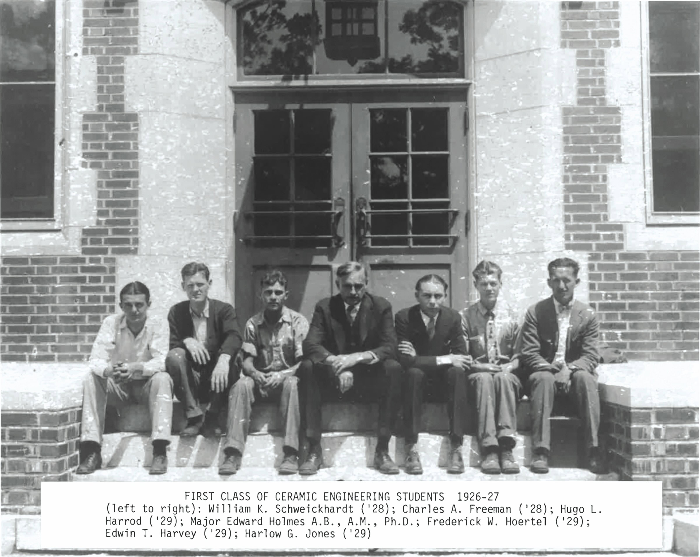 A group of seven young men and one older man sitting on steps outside a brick building, labeled as ceramic engineering studen.
