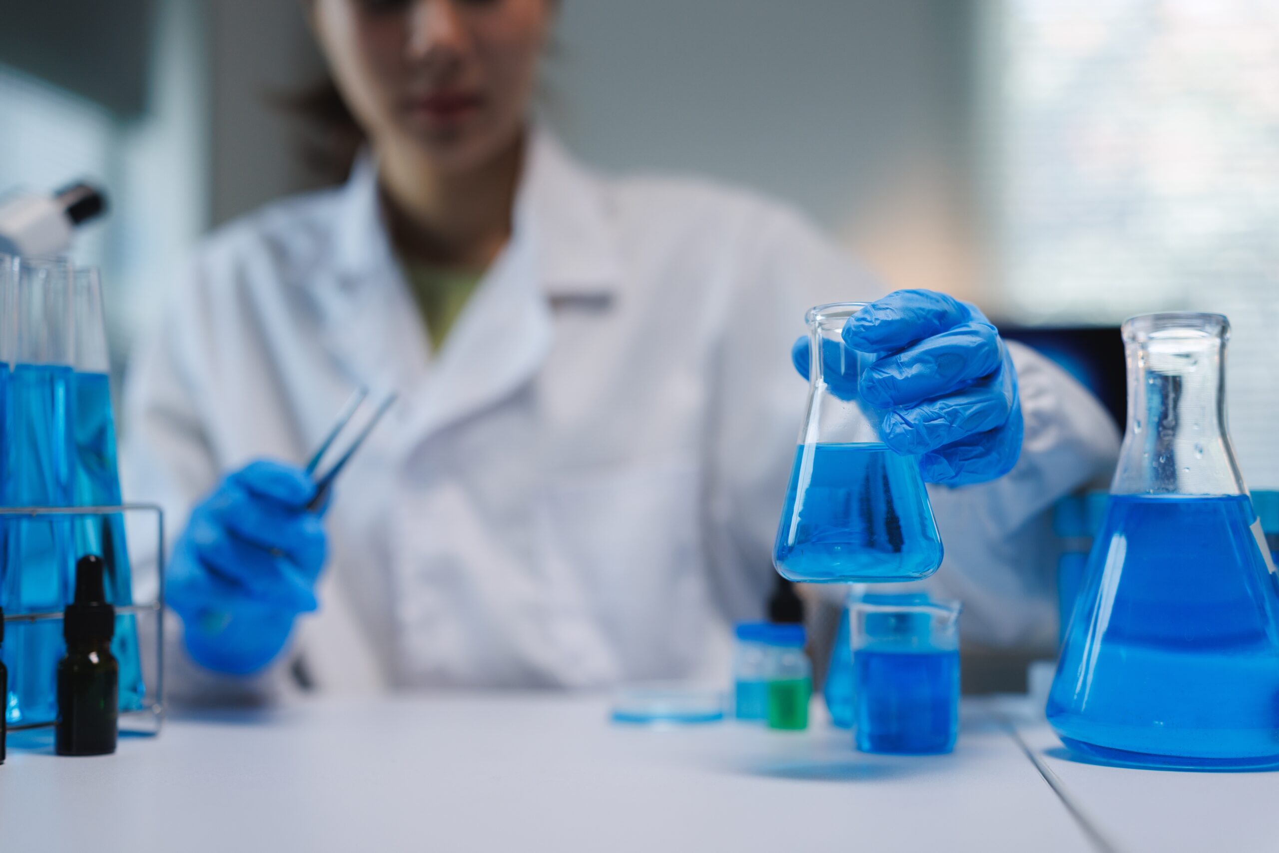 A scientist in a lab wearing blue gloves conducts experiments with blue liquids in glassware.