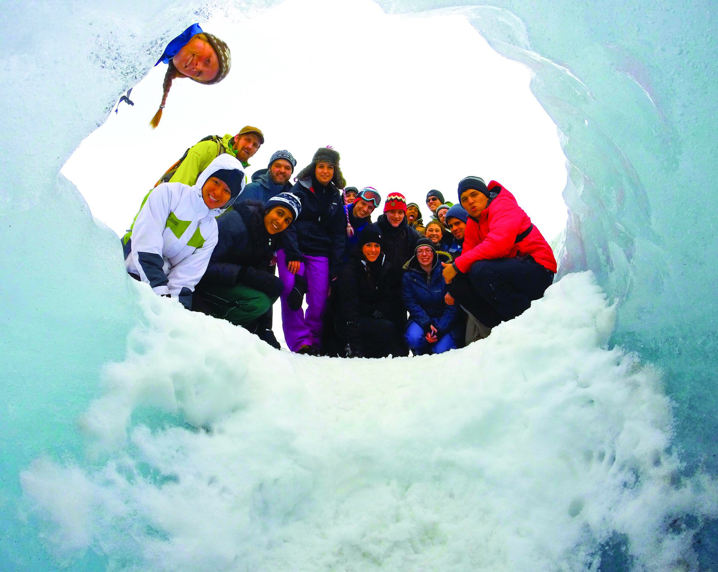 Exploring an ice cave with a group of people in winter gear, surrounded by snow and ice formations.