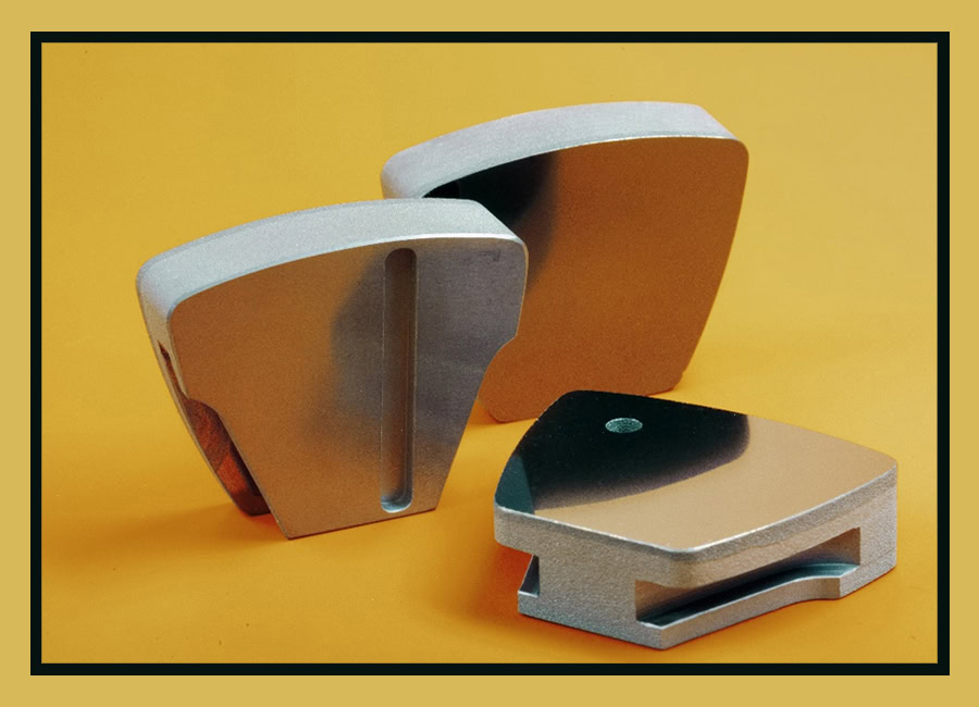 Three ceramic or metallic industrial components with smooth surfaces and geometric shapes on a yellow background.