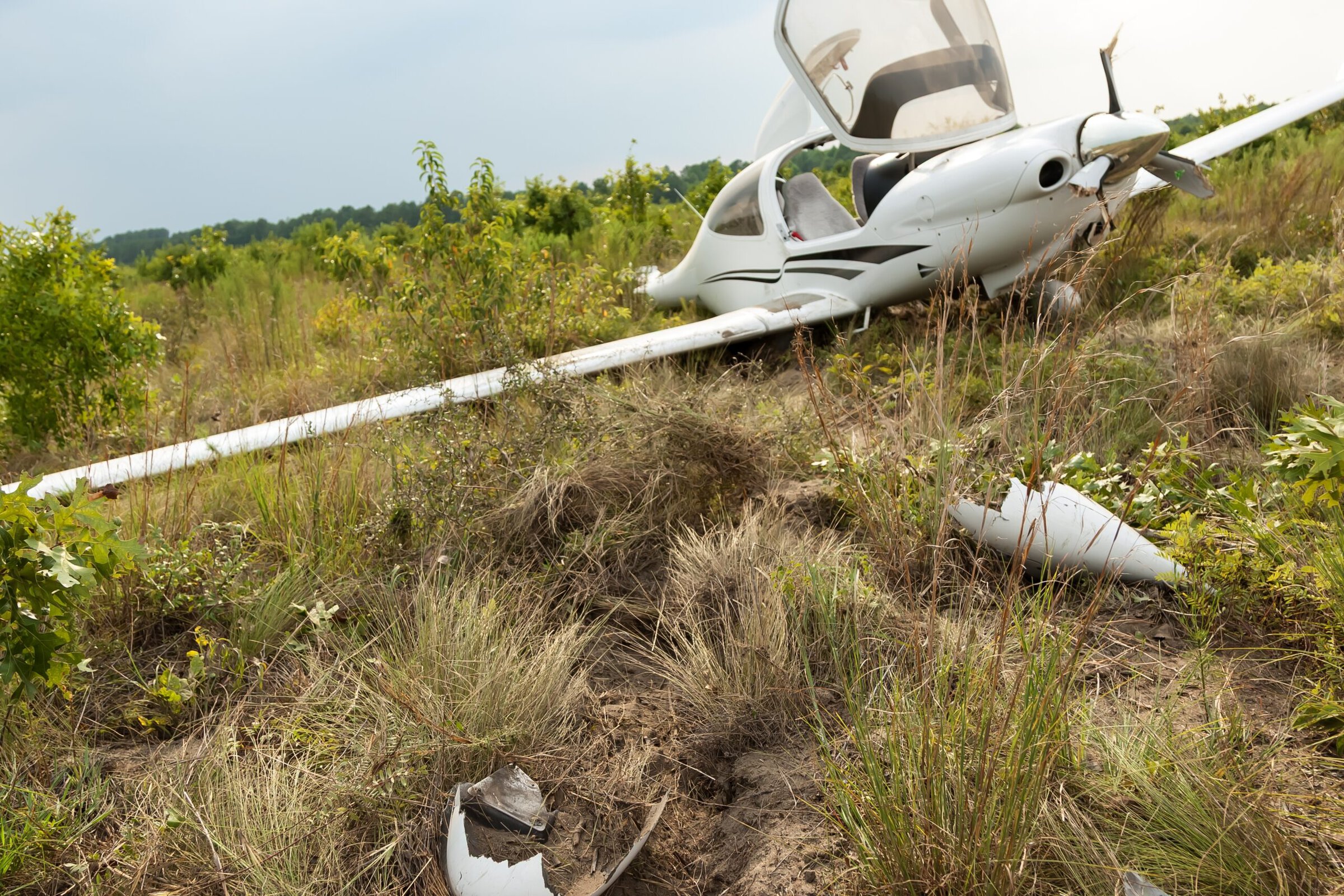 Small plane crash in grassy field with wreckage and damaged fuselage.