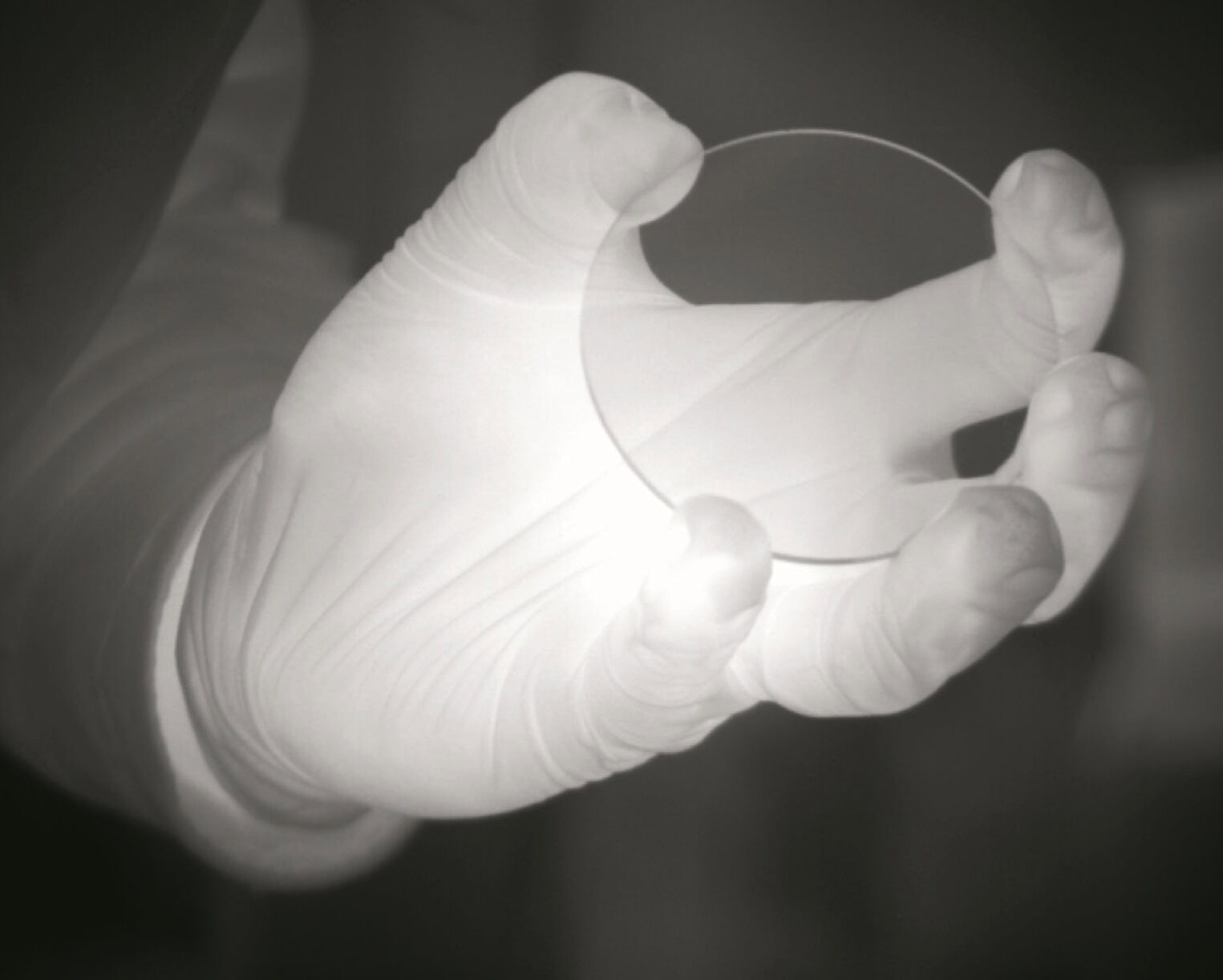 Close-up of a gloved hand holding a transparent alumina disk