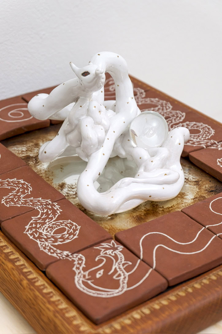 Ceramic sculpture of a dragon coiled around a glass orb, set on a decorative tile base with dragon motifs.